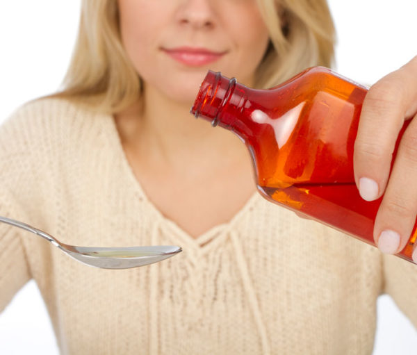 Woman getting ready to pour liquid from a bottle into a measuring spoon.