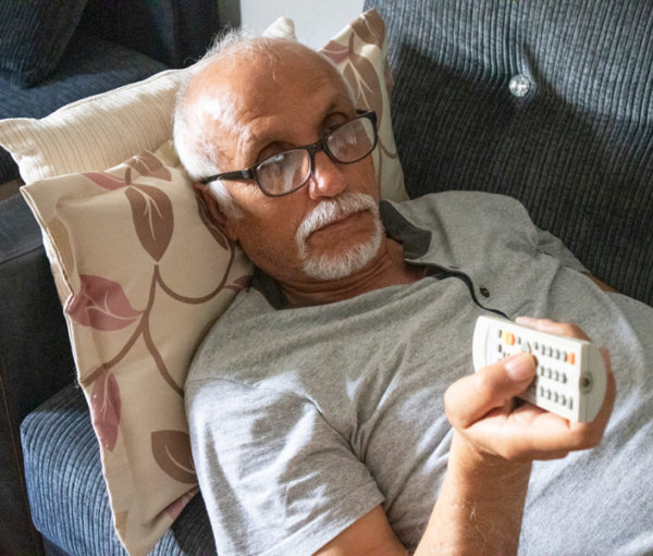Senior man laying on couch with television remote.