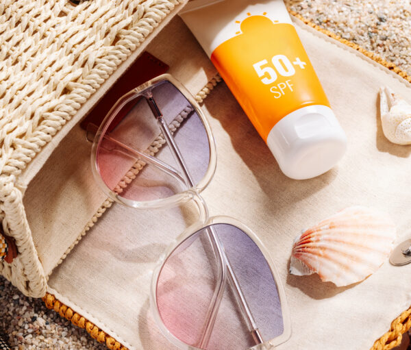 Sunscreen and glasses in a wicker straw bag on a sandy beach