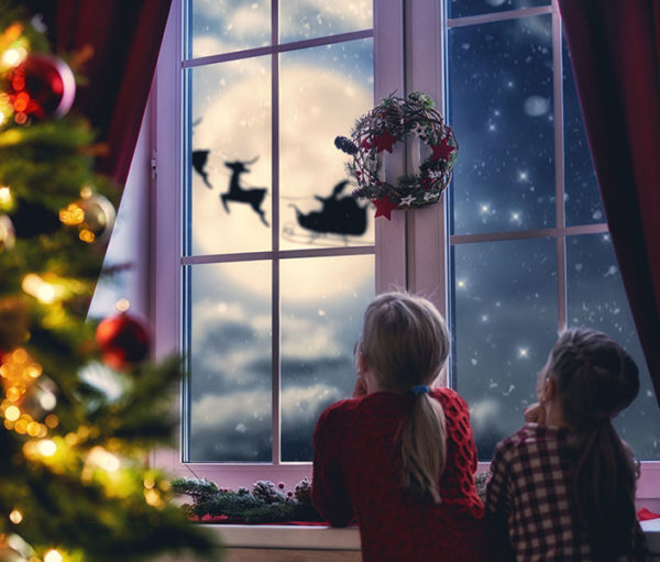 children looking out window at Santa and reindeer against a full moon